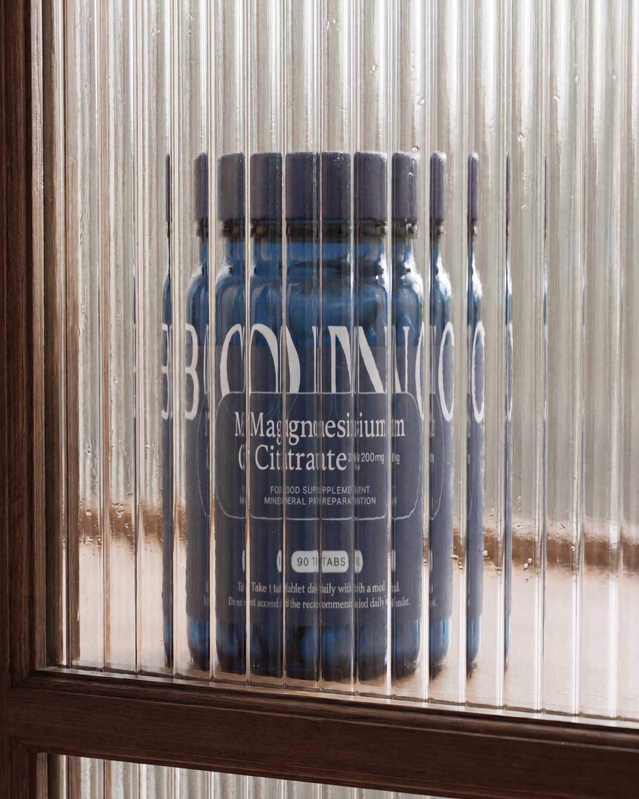 Un bote de BONO Supplements Citrato de magnesio detrás de un cristal acanalado